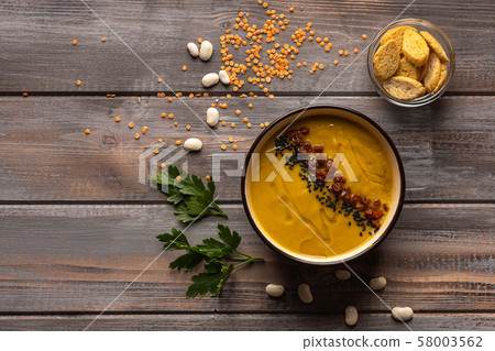 Cream soup with a mixture of beans and spices on a wooden background. near a vase with crackers. On Cream soup with a mixture of beans and spices on a wooden background. near a vase with crackers. On 58003562