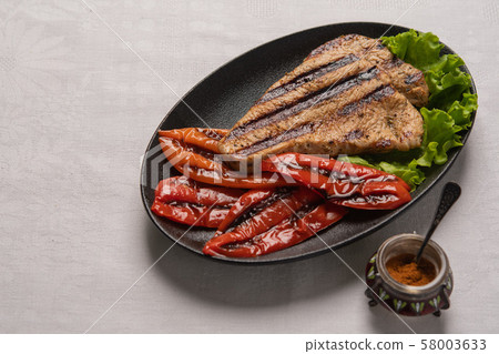 Grilled Turkey breast steak with baked peppers and lettuce leaves in a black plate on a light linen 58003633