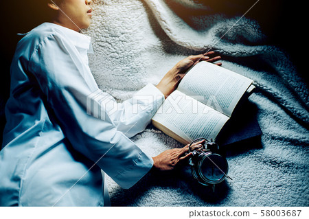 Irritated young woman putting her alarm clock off Irritated young woman putting her alarm clock off 58003687