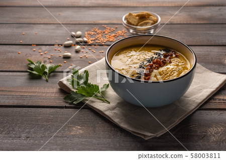 Cream soup with a mixture of beans and spices on a napkin on a wooden background. Near crackers and Cream soup with a mixture of beans and spices on a napkin on a wooden background. Near crackers and 58003811