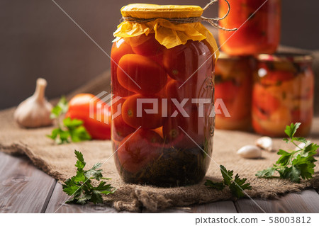 Homemade jars of pickled tomatoes on a rustic wooden background. Pickled and canned product. Next Homemade jars of pickled tomatoes on a rustic wooden background. Pickled and canned product. Next 58003812