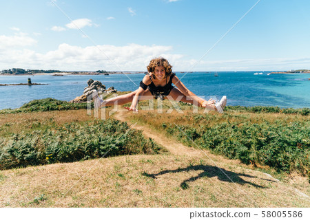 Smiling and attractive young woman jumping in the coast Smiling and attractive young woman jumping in the coast 58005586