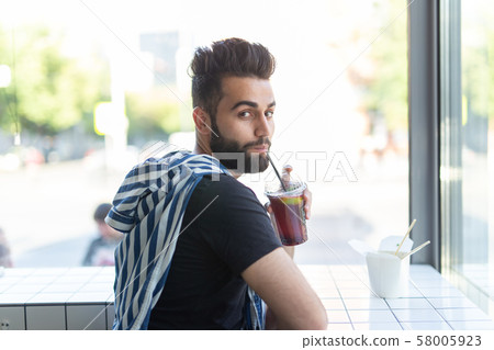 Positive young stylish guy drinking juice in a cafe during a break at work. The concept of rest and Positive young stylish guy drinking juice in a cafe during a break at work. The concept of rest and 58005923