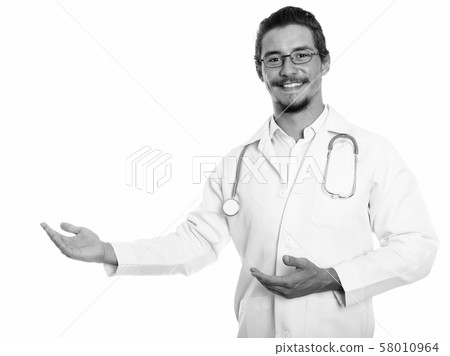 Studio shot of young happy man doctor smiling while showing something isolated against white Studio shot of young happy man doctor smiling while showing something isolated against white 58010964
