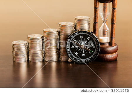 Stack of coins with hourglass and compass on wood Stack of coins with hourglass and compass on wood 58011976
