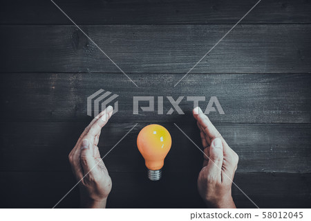 Hands protect yellow light bulb on wood table 58012045