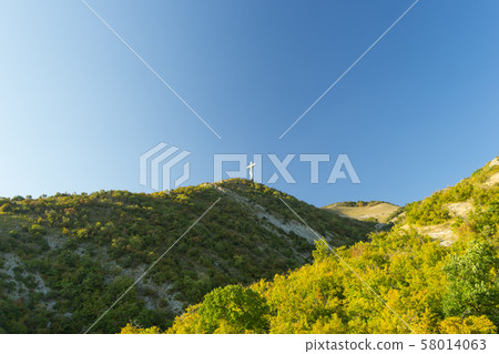 Green hills of Caucasian mountains with orthodox worship cross on top of one of them. Beautiful 58014063