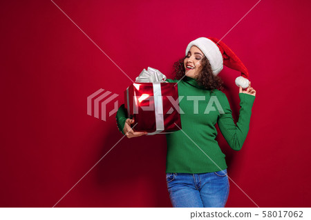 Beautiful fashion woman in santa claus hat. Warm Christmas sweater holding gift box on. 58017062