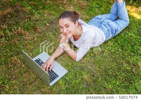 Young woman lying on green grass lawn in city park Young woman lying on green grass lawn in city park 58017074