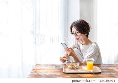 Woman eating breakfast while looking at smartphone Woman eating breakfast while looking at smartphone 58036894