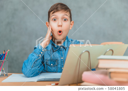 Cute school kid in blue jeans t-shirt sitting at table full of books. Looking at the camera with Cute school kid in blue jeans t-shirt sitting at table full of books. Looking at the camera with 58041805