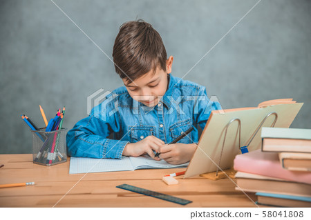 Young concentrated school kid in blue jeans t-shirt writing sitting at table with books. Young concentrated school kid in blue jeans t-shirt writing sitting at table with books. 58041808
