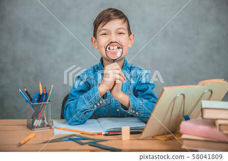 Funny small schoolkid playing around with a loupe, holding it in front of his mouth, making Funny small schoolkid playing around with a loupe, holding it in front of his mouth, making 58041809