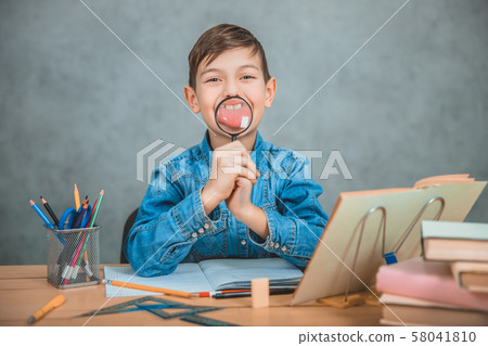 Funny small schoolkid playing around with a loupe, holding it in front of his mouth, making Funny small schoolkid playing around with a loupe, holding it in front of his mouth, making 58041810