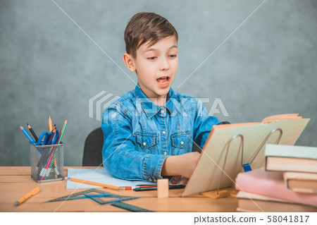 Inquisitive little boy is looking through magnifying glass at something in his book like detective. Inquisitive little boy is looking through magnifying glass at something in his book like detective. 58041817