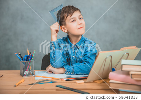 Cute handsome schoolkid looking thoughtfully at the camera, putting the triangle on his head. Cute handsome schoolkid looking thoughtfully at the camera, putting the triangle on his head. 58041818