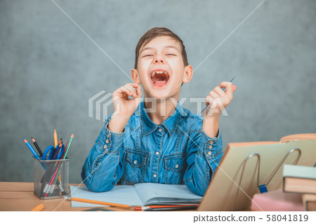 Funny schoolboy sitting at the desk full of school supplies, laughing. Funny schoolboy sitting at the desk full of school supplies, laughing. 58041819