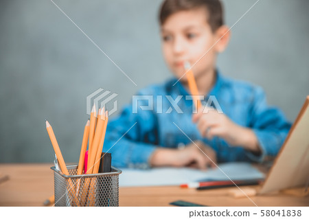 Basket with pencils and highlighters on the forefront. Concentrated schoolboy thinking on the Basket with pencils and highlighters on the forefront. Concentrated schoolboy thinking on the 58041838