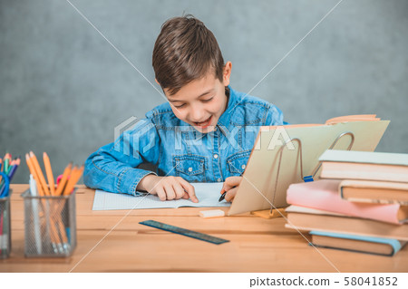 Cute schoolboy is smiling happily, writing something exciting in his copybook. 58041852