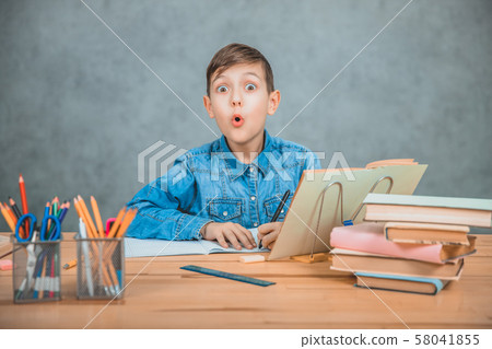 Young concentrated school kid in blue jeans t-shirt wriring sitting at table full of books. Looking Young concentrated school kid in blue jeans t-shirt wriring sitting at table full of books. Looking 58041855