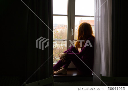 girl sitting on a windowsill and looking at the girl sitting on a windowsill and looking at the 58041935