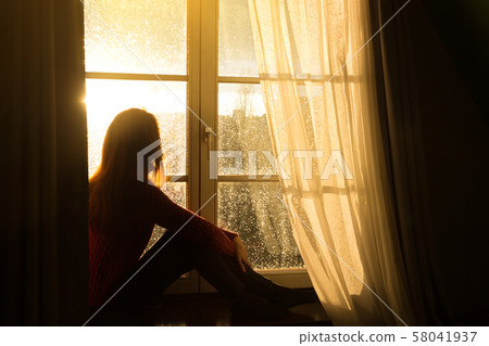 girl sitting on a windowsill and looking at the 58041937