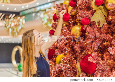 Woman hangs a decoration on the red Christmas tree. Red Christmas tree on the background of lights Woman hangs a decoration on the red Christmas tree. Red Christmas tree on the background of lights 58042227