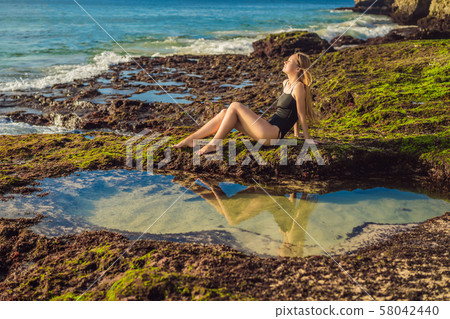 Young woman tourist on Pantai Tegal Wangi Beach sitting in a bath of sea water, Bali Island Young woman tourist on Pantai Tegal Wangi Beach sitting in a bath of sea water, Bali Island 58042440