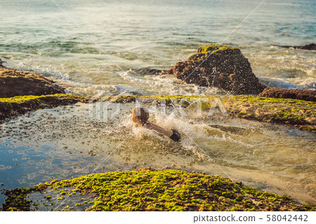 Boy tourist on Pantai Tegal Wangi Beach sitting in a bath of sea water, Bali Island, Indonesia. Bali 58042442
