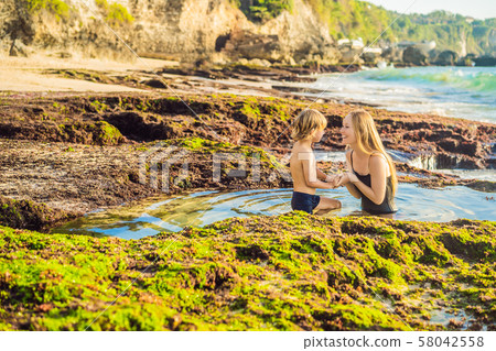 Mother and son tourists on Pantai Tegal Wangi Beach sitting in a bath of sea water, Bali Island 58042558