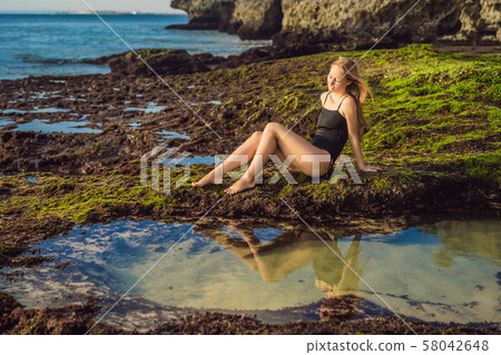 Young woman tourist on Pantai Tegal Wangi Beach sitting in a bath of sea water, Bali Island Young woman tourist on Pantai Tegal Wangi Beach sitting in a bath of sea water, Bali Island 58042648