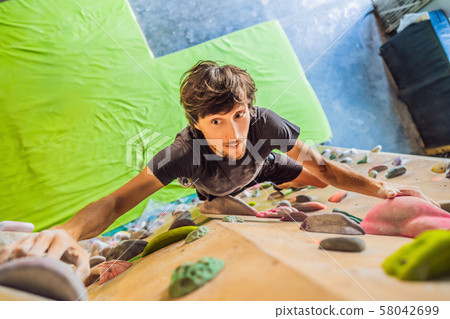 Muscular man practicing rock-climbing on a rock wall indoors 58042699