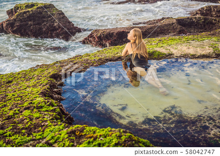 Young woman tourist on Pantai Tegal Wangi Beach sitting in a bath of sea water, Bali Island Young woman tourist on Pantai Tegal Wangi Beach sitting in a bath of sea water, Bali Island 58042747