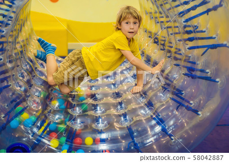 Cute little boy, playing in Zorb a rolling plastic cylinder ring with a hole in the middle, intdoor Cute little boy, playing in Zorb a rolling plastic cylinder ring with a hole in the middle, intdoor 58042887