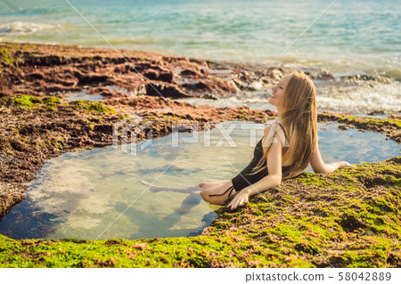 Young woman tourist on Pantai Tegal Wangi Beach sitting in a bath of sea water, Bali Island Young woman tourist on Pantai Tegal Wangi Beach sitting in a bath of sea water, Bali Island 58042889
