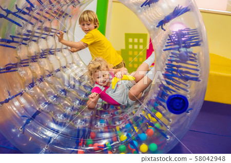 Cute little boy and girl playing in Zorb a rolling plastic cylinder ring with a hole in the middle 58042948