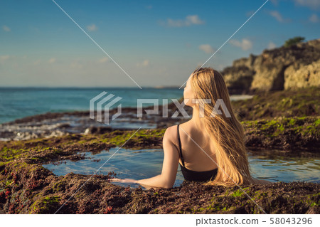 Young woman tourist on Pantai Tegal Wangi Beach sitting in a bath of sea water, Bali Island Young woman tourist on Pantai Tegal Wangi Beach sitting in a bath of sea water, Bali Island 58043296