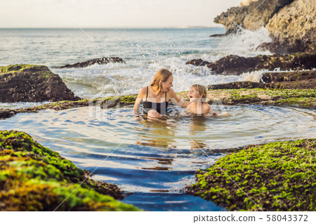 Mother and son tourists on Pantai Tegal Wangi Beach sitting in a bath of sea water, Bali Island 58043372