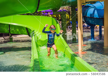 Happy boy on water slide in a swimming pool having fun during summer vacation in a beautiful Happy boy on water slide in a swimming pool having fun during summer vacation in a beautiful 58043586