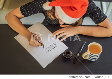 Merry christmas and a happy new year. Calligrapher Young Woman writes phrase on white paper Merry christmas and a happy new year. Calligrapher Young Woman writes phrase on white paper 58044005