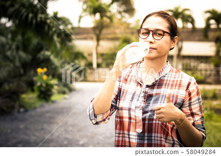 Women wearing glasses drinking water in plastic bottles on the roadside Women wearing glasses drinking water in plastic bottles on the roadside 58049284