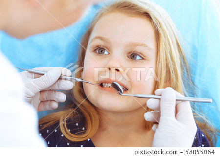 Little baby girl sitting at dental chair with open mouth during oral check up while doctor. Visiting Little baby girl sitting at dental chair with open mouth during oral check up while doctor. Visiting 58055064