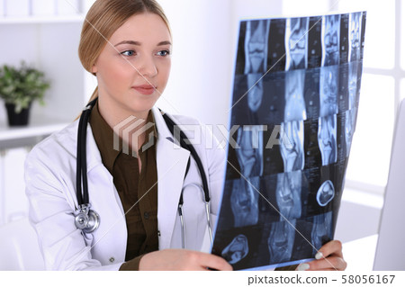 Doctor woman examining x-ray picture near window in hospital. Surgeon or orthopedist at work Doctor woman examining x-ray picture near window in hospital. Surgeon or orthopedist at work 58056167