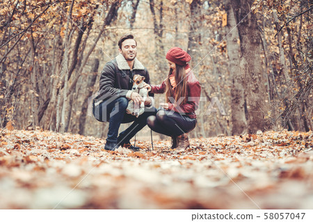 Woman and man in the fall strolling with their dog in the park 58057047