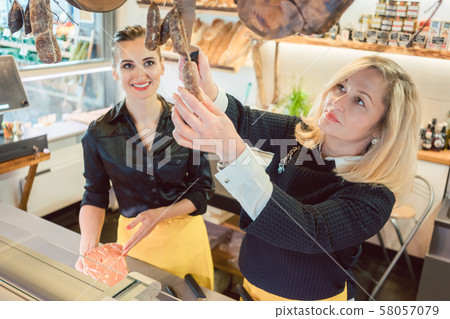 Shop assistant women selling cheese and meats in deli Shop assistant women selling cheese and meats in deli 58057079