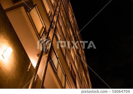 A shot of a real estate agent looking up at an apartment at night 58064709