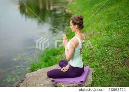 A young sports girl practices yoga on a green lawn A young sports girl practices yoga on a green lawn 58068721