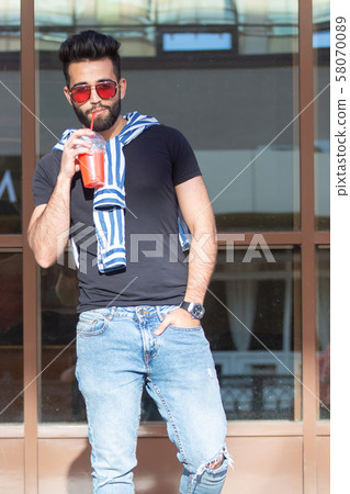 Handsome cheerful young arabian student with a stylish mustache and a beard with juice in his hands 58070089