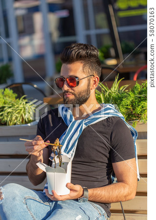 Handsome young arab man are holding wooden sticks chinese noodle. Delicious asian cuisine concept. 58070163