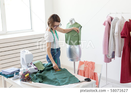 Young pretty girl seamstress designer with glasses and a measuring tape makes a new product with the Young pretty girl seamstress designer with glasses and a measuring tape makes a new product with the 58071627